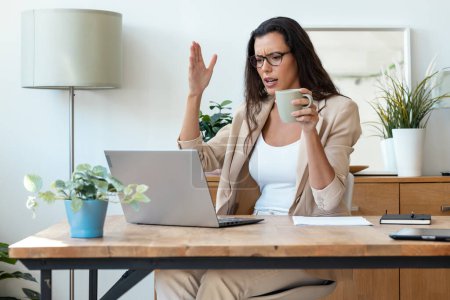 Téléchargez les photos : Prise de vue d'une femme d'affaires en colère inquiète travaillant avec un ordinateur portable tout en ayant des problèmes dans une start-up moderne - en image libre de droit