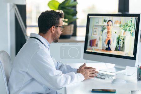 Photo for Shot of mature male doctor talking in a video call with computer in the consultation. - Royalty Free Image