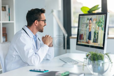 Photo for Shot of mature male doctor talking in a video call with computer in the consultation. - Royalty Free Image