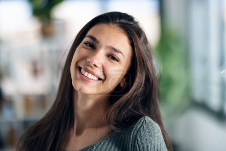 Photo for Portrait of smiling young woman posing while looking at camera in the living room at home. - Royalty Free Image
