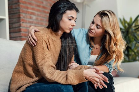 Photo for Shot of pretty young woman supporting and comforting her sad friend while sitting on the sofa at home. - Royalty Free Image