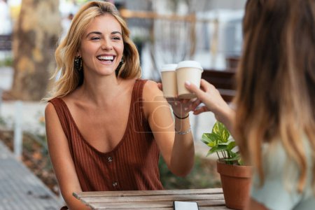 Téléchargez les photos : Tourné de deux amis attrayants dégustant un café ensemble tout en parlant et en riant assis sur la terrasse d'un bar. - en image libre de droit