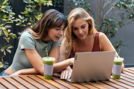 Foto de Shot of two happy friends sharing a brunch together while working with laptop in the eco coffee shop terrace. - Imagen libre de derechos