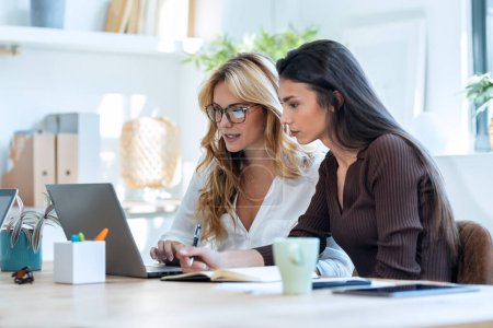 Photo for Shot of two elegant attractive businesswomen talking while working together with laptop in a modern startup - Royalty Free Image