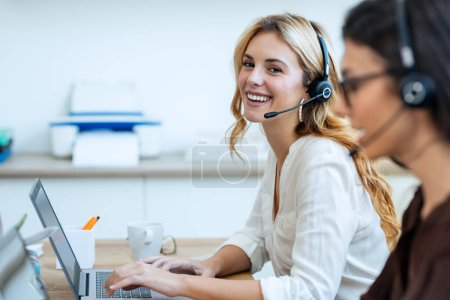 Téléchargez les photos : Prise de vue de femmes d'affaires attrayantes qui travaillent avec des ordinateurs portables tout en parlant avec un écouteur sur un lieu de coworking. - en image libre de droit