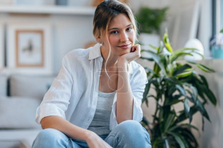 Téléchargez les photos : Portrait de belle femme regardant la caméra tout en étant assis sur le canapé dans le salon à la maison - en image libre de droit