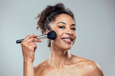 Foto de Fotografía de una hermosa mujer joven haciendo maquillaje mientras mira a la cámara en blanco aislado - Imagen libre de derechos