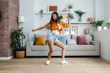 Aufnahme einer lustig motivierten Frau, die tanzt und Musik hört, während sie das Haus fegt
