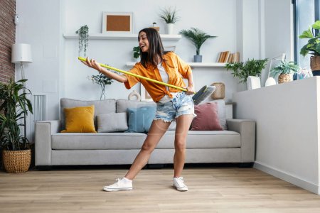 Aufnahme einer lustig motivierten Frau, die tanzt und Musik hört, während sie das Haus fegt