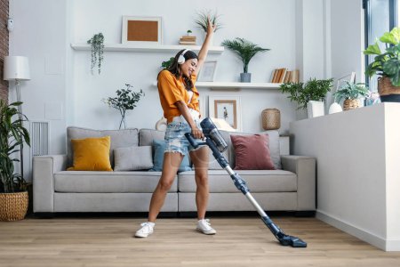 Photo for Shot of young happy woman listening and dancing to music while cleaning the living room floor with a vaccum cleaner - Royalty Free Image