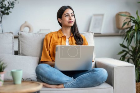 Photo for Shot of confident young woman working with her laptop while sitting on a couch at home - Royalty Free Image