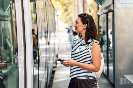 Foto de mujer segura usando su teléfono móvil mientras espera el tranvía en la estación