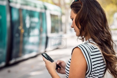 Foto de mujer segura usando su teléfono móvil mientras espera el tranvía en la estación