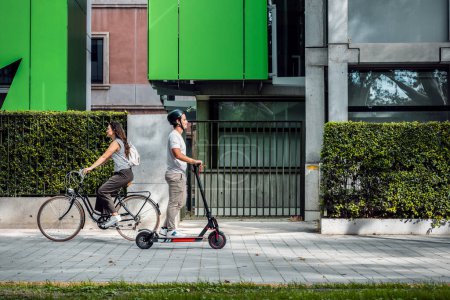 Foto de Un disparo de mujer alegre en bicicleta cruza a un hombre concentrado en un scooter eléctrico por la ciudad - Imagen libre de derechos