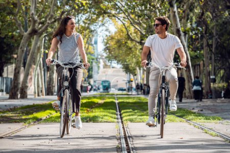 Photo for Shot of happy loving couple cycling while looking each other in the city - Royalty Free Image