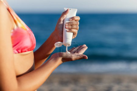 Téléchargez les photos : Gros plan de la jeune femme appliquant de la crème solaire sur elle-même pour protéger sa peau du soleil à la plage - en image libre de droit