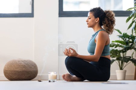 Téléchargez les photos : Prise de vue de jeune femme sportive faisant du yoga et des exercices hypopressifs tout en restant en position lotus dans le salon à la maison. - en image libre de droit