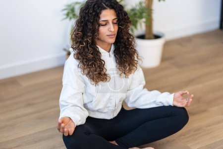 Téléchargez les photos : Prise de vue de jeune femme sportive faisant des exercices de yoga tout en restant en position lotus dans le salon à la maison. - en image libre de droit