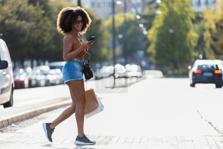 Téléchargez les photos : Prise de vue de belle femme utilisant un smartphone lors de la traversée d'un passage de zèbre dans la ville - en image libre de droit