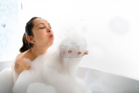 Téléchargez les photos : Salle de bain Détente et bien-être. Femme soufflant des bulles de mousse de savon - en image libre de droit