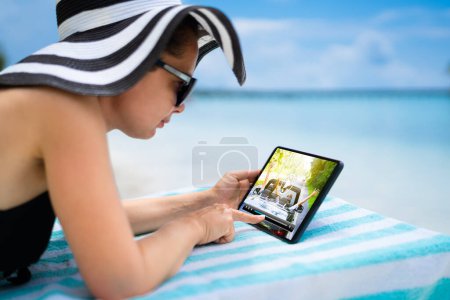 Téléchargez les photos : Femme Regarder un film de télévision ou une vidéo sur tablette à la plage - en image libre de droit