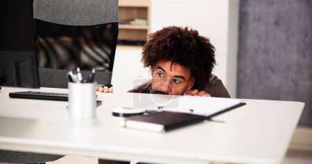Foto de Hombre asustado escondiéndose detrás del escritorio de la oficina en la habitación - Imagen libre de derechos