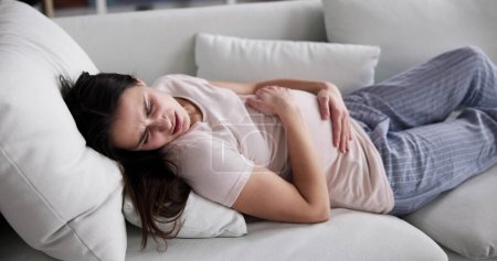 Foto de Young Pregnant Woman Suffering From Stomach Ache At Home - Imagen libre de derechos
