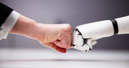 Téléchargez les photos : Robot et main humaine faisant coup de poing sur fond gris - en image libre de droit