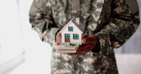 Téléchargez les photos : Programme de la SCRA. Armée militaire homme en uniforme tenant une nouvelle maison - en image libre de droit