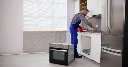 Photo for Young Repairman Installing Induction Cooker In Kitchen - Royalty Free Image