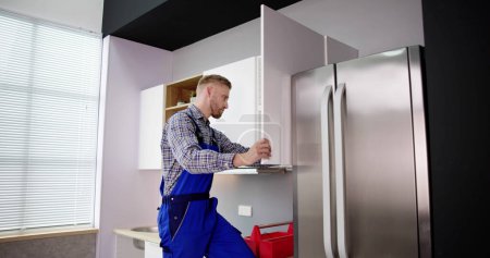 Téléchargez les photos : Male Carpenter Assembling White Cabinet On Wall In Kitchen - en image libre de droit