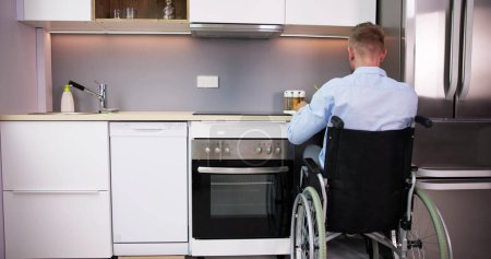 Foto de Hombre con discapacidad sentado en silla de ruedas preparando comida en la cocina - Imagen libre de derechos