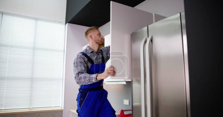 Foto de Carpintero masculino que monta el gabinete blanco en la pared en la cocina - Imagen libre de derechos