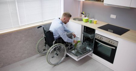 Foto de Persona con discapacidad en silla de ruedas usando lavavajillas en la cocina - Imagen libre de derechos
