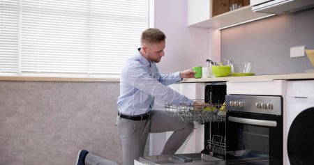 Téléchargez les photos : Jeune homme prenant verre à boire du lave-vaisselle dans la cuisine - en image libre de droit