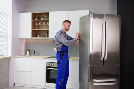 Téléchargez les photos : Réfrigérateur de réparation de travailleur masculin avec tournevis dans la maison - en image libre de droit