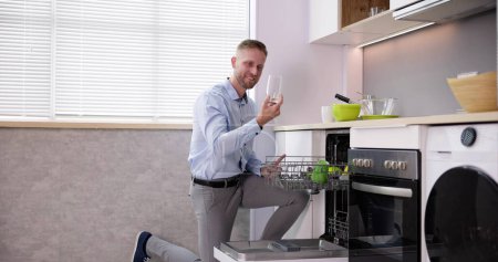 Téléchargez les photos : Jeune homme prenant verre à boire du lave-vaisselle dans la cuisine - en image libre de droit