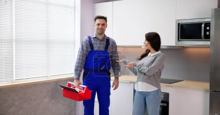 Foto de Mujer feliz presentando reparador masculino en la sala de cocina - Imagen libre de derechos