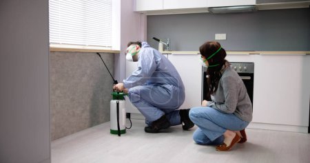 Téléchargez les photos : Femme regardant Exterminateur travailleur pulvérisation insecticide chimique pour la lutte antiparasitaire termite dans la cuisine de la maison - en image libre de droit