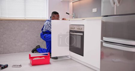 Foto de Reparador en overoles Reparación de la bisagra del gabinete en la cocina - Imagen libre de derechos