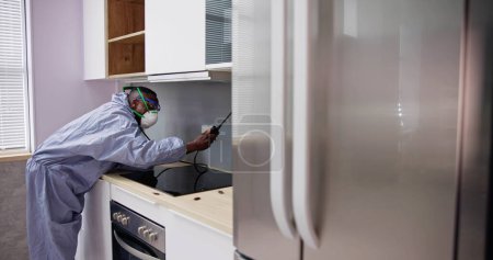 Photo for Man Showing At Pest Control Worker Spraying Insecticide On Shelf Of Domestic Kitchen - Royalty Free Image