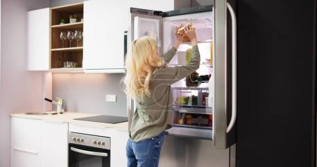 Photo for Young Woman Eating Sandwich In Front Of Refrigerator - Royalty Free Image