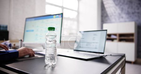 Photo for Water Bottle On Desk And Man In Background Using Computer - Royalty Free Image