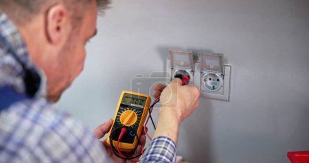 Photo for Male Electrician Checking Voltage Of Socket With Multimeter In House - Royalty Free Image