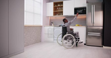 Foto de Hombre discapacitado usando la herramienta del grabador para controlar el microondas en la cocina - Imagen libre de derechos