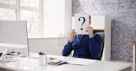 Téléchargez les photos : Homme d'affaires tenant du papier avec un point d'interrogation devant le visage au bureau - en image libre de droit