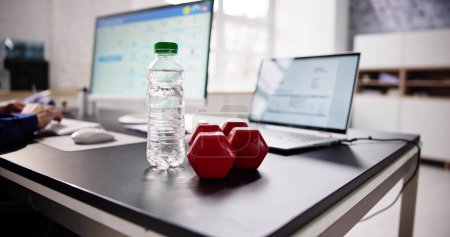 Photo for Close-up Of Water Bottle And Dumbbell In Front Of Businessperson Working In Office - Royalty Free Image