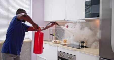Photo for Man Using Fire Extinguisher To Stop Fire On Burning Cooking Pot In The Kitchen - Royalty Free Image