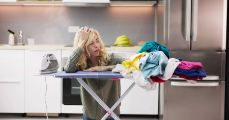 Foto de Mujer joven agotada mientras plancha ropa en casa - Imagen libre de derechos