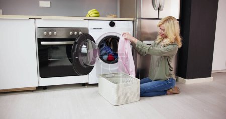 Foto de Mujer oliendo ropa limpia cerca de la lavadora electrónica en la sala de lavandería - Imagen libre de derechos